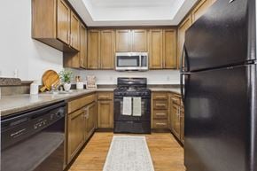 Los Angeles apartment for rent - A black refrigerator stands in a kitchen with wooden cabinets and a black oven.