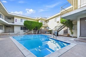 Burbank apartment for rent - A swimming pool in front of a building with a blue sky and clouds in the background.