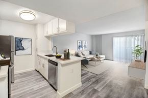 Northridge apartment for rent - A modern kitchen with a refrigerator on the left and a dining area with a white couch and a coffee table.