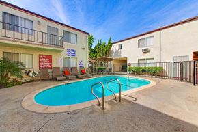 Van Nuys apartment for rent - A pool surrounded by a fence and chairs in front of a building.