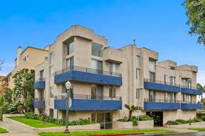 Los Angeles apartment for rent - A large, modern building with blue balconies and a red curb.