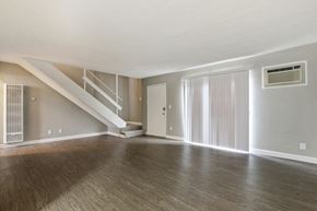 Glendora apartment for rent - Living room with air conditioning on the right, wood-style flooring, vertical blinds, carpeted staircase to the second floor