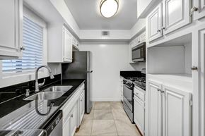 Studio City apartment for rent - a kitchen with white cabinets and black counter tops and a sink