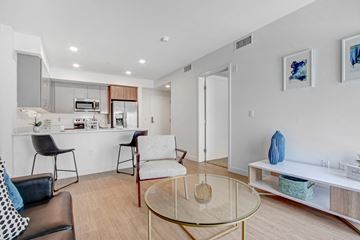 Reseda apartment for rent - A modern living room with a glass coffee table and a kitchen area in the background.