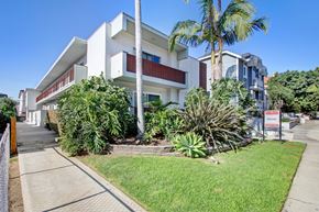 Los Angeles apartment for rent - A white building with a red balcony is surrounded by greenery.