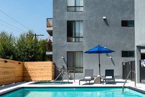 Los Angeles apartment for rent - a pool with a blue umbrella and two chairs in front of a gray building