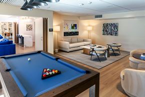 Canoga Park apartment for rent - A pool table with a blue cloth and a rack of balls is in the foreground of a room with a couch, chairs, and a painting on the wall.