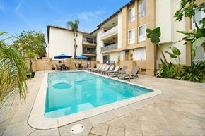 Sherman Oaks apartment for rent - A swimming pool in a courtyard surrounded by chairs and umbrellas.