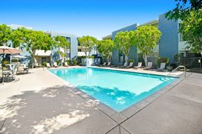 Northridge apartment for rent - a swimming pool in front of a building with chairs and trees