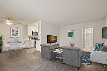 Los Angeles apartment for rent - A living room with a grey couch, a grey ottoman, a white dining table with four chairs, a television, and a plant.