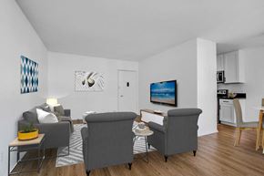 Studio City apartment for rent - A living room with a grey couch, a grey chair, a small table, a potted plant, a painting, a lamp, a television, and a kitchen area with a white counter and a white oven.