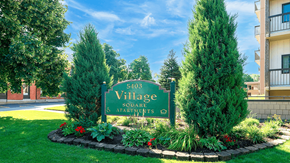 Williamsville apartment for rent - A sign for Village Square Apartments surrounded by greenery.