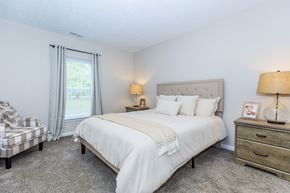 Kent apartment for rent - A bedroom with a large bed, a nightstand with a lamp, and a chair with a blanket on it.