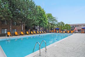 Naperville apartment for rent - A pool with orange chairs and trees in the background.