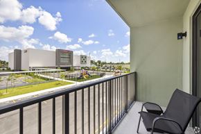 Miami apartment for rent - A balcony with a chair and a view of a parking lot and buildings.