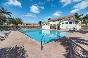 Homestead townhouse for rent - A large swimming pool surrounded by a brick patio and a white building in the background.