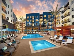 Laguna Niguel apartment for rent - A large swimming pool surrounded by lounge chairs and umbrellas in front of a multi-story building.