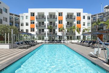 Orange apartment for rent - A large swimming pool in front of a white building with orange and gray accents.