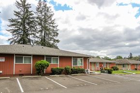Lakewood apartment for rent - A parking lot in front of a red building with trees in the background.
