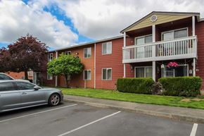 Puyallup apartment for rent - A silver car is parked in a parking lot in front of a red building.