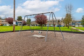 Chehalis apartment for rent - A playground with a swing set in the foreground and apartment buildings in the background.