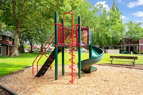 Mcminnville apartment for rent - A playground with a red and green slide and a brown bench.
