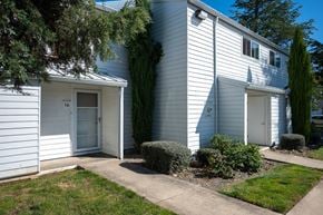 Albany apartment for rent - A white house with a grey roof and a green tree in front.