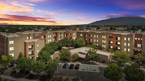 Albuquerque apartment for rent - A sunset view of a large apartment complex with a parking lot in front.