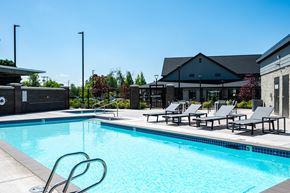 Milwaukie apartment for rent - a swimming pool with chairs and a building in the background