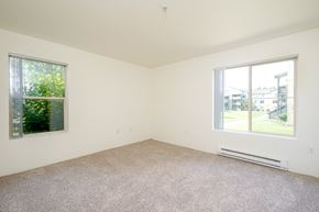 Hillsboro apartment for rent - A room with a carpet floor, a window with a view of a building and trees outside, and a wall-mounted air conditioner.