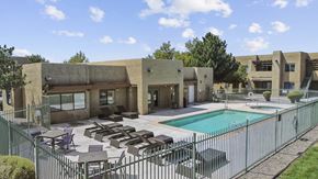 Albuquerque apartment for rent - A pool surrounded by a fence and chairs outside a building.