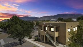 Albuquerque apartment for rent - A modern building with a staircase leading to the entrance is surrounded by trees and has a mountain range in the background.