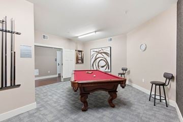 Huntsville apartment for rent - A pool table is in the middle of a room with a chair and a clock on the wall.