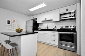 Cocoa apartment for rent - a kitchen with white cabinets and stainless steel appliances and a black counter top
