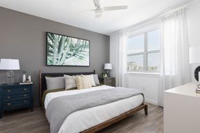 Orlando apartment for rent - a bedroom with a ceiling fan, large window, wood-style floors, and model furnishings