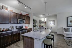 Burleson apartment for rent - Kitchen island with granite countertop, double basin sink, hanging light fixture, barstools, dark wood cabinetry and stainless appliances