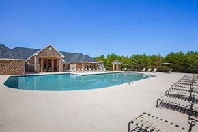 Greensboro apartment for rent - A large swimming pool is surrounded by a concrete patio and a house with a stone wall at Ethan Pointe Apartments, Greensboro, 27215