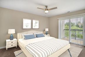 Gaithersburg apartment for rent - A virtually staged bedroom with gray walls with white trim, dark gray carpet throughout, and sliding glass door with vertical blinds leading to the outside patio/balcony area.
