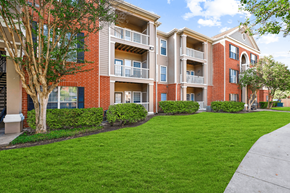 Houston apartment for rent - A red brick apartment building with green bushes and trees.