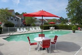 Virginia Beach apartment for rent - Community swimming pool with four red chairs and a red umbrella surrounding a table