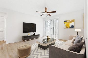 Charlotte apartment for rent - A living room with a brown ottoman, a grey couch, a black and white rug, a wooden floor, a flat screen TV, a ceiling fan, and a painting on the wall.