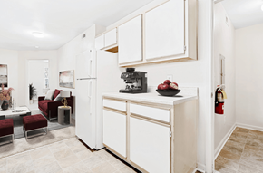 High Point apartment for rent - Virtually staged kitchen with tile floors, white appliances, and wood cabinets. Living room in background with maroon accent furniture.