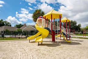 Fort Myers apartment for rent - Blue Red and Yellow Playground on Sand with Building Exterior and Treeline in the Background