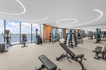 Sunlight-flooded fitness center with floor-to-ceiling glass walls featuring the perfect mix of top-of-the-line cardio, strength, and functional training equipment pickleball yoga and movement studio