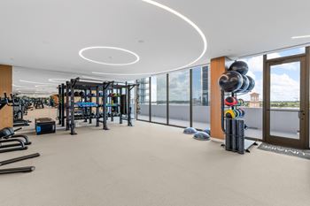 Sunlight-flooded fitness center with floor-to-ceiling glass walls featuring the perfect mix of top-of-the-line cardio, strength, and functional training equipment pickleball yoga and movement studio