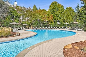 A large outdoor swimming pool surrounded by trees and chairs.