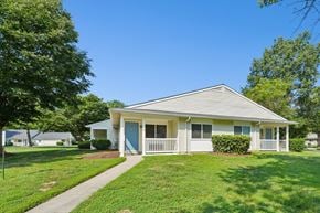Waldorf apartment for rent - A house with a blue door and white trim is surrounded by green grass and trees.