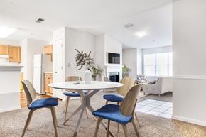 Canton apartment for rent - Vacant staged living room with wall-to-wall carpet. Door that lead to patio, vaulted ceiling and fireplace. View of kitchen in the background with white appliances and brown cabinets. Dinning table and couches set up in the back with mounted tv above the fireplace.
