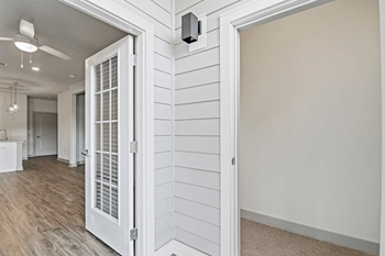 A white door with a window is open to a room with wood flooring.
