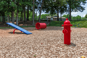 A red fire hydrant sits on a playground with a blue bench and two red barrels.
